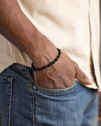 Pulsera de Espinela Negra y Turmalina Negra puesta, la mano dentro del bolsillo de un pantalón de mezclilla