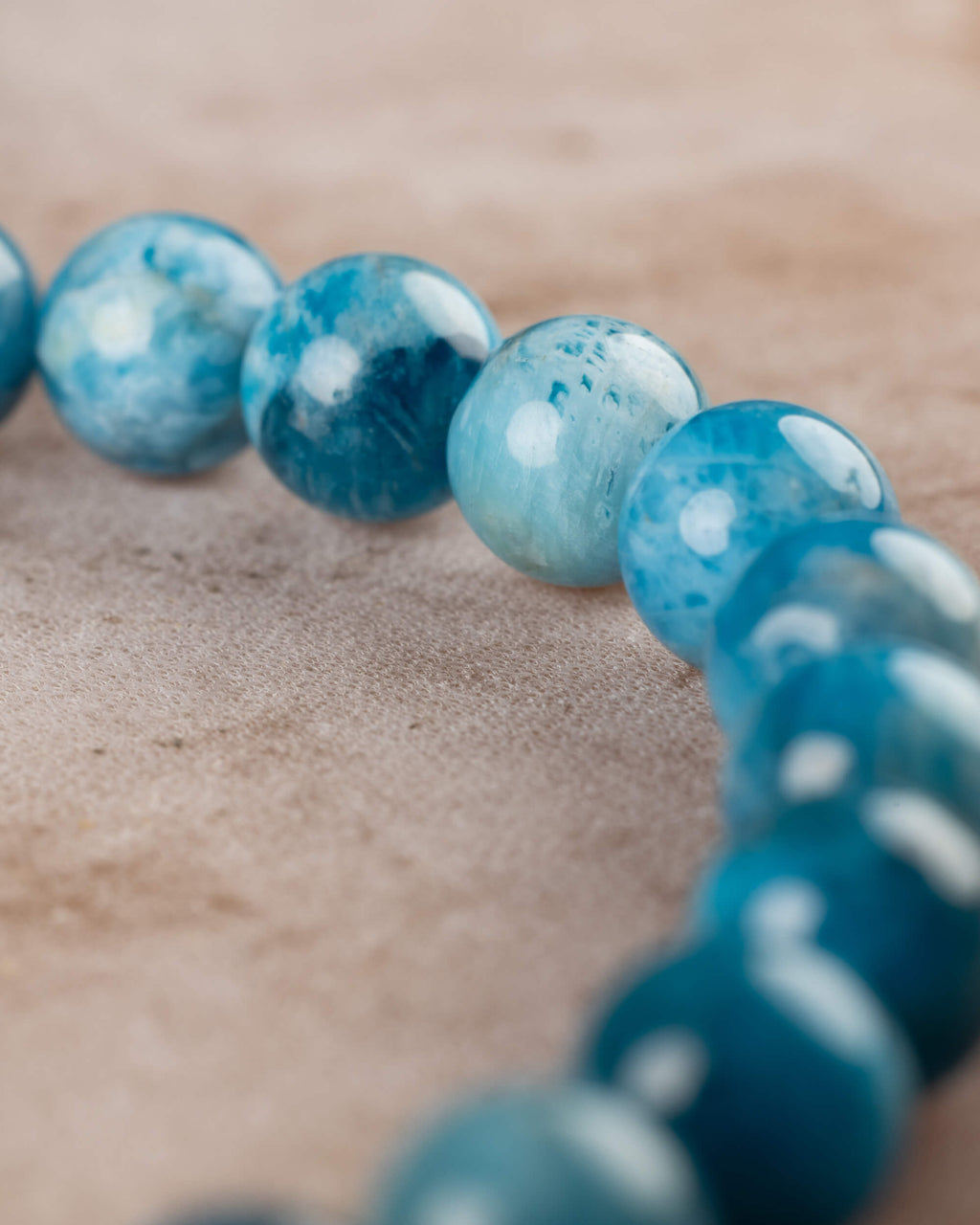 Cuentas de Apatita Azul en perspectiva con la pulsera desenfocada al fondo