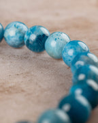 Cuentas de Apatita Azul en perspectiva con la pulsera desenfocada al fondo