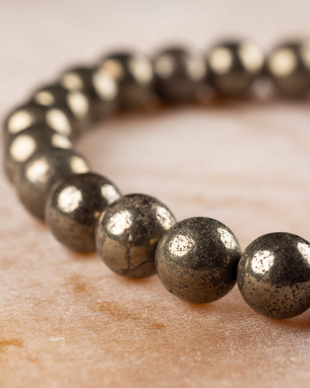 Pulsera de Pirita en perspectiva, cuentas doradas en curva sobre superficie clara