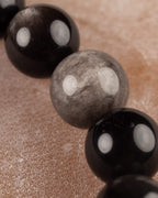 Detalle macro de cuenta gris de Obsidiana Plateada rodeada de cuentas negras