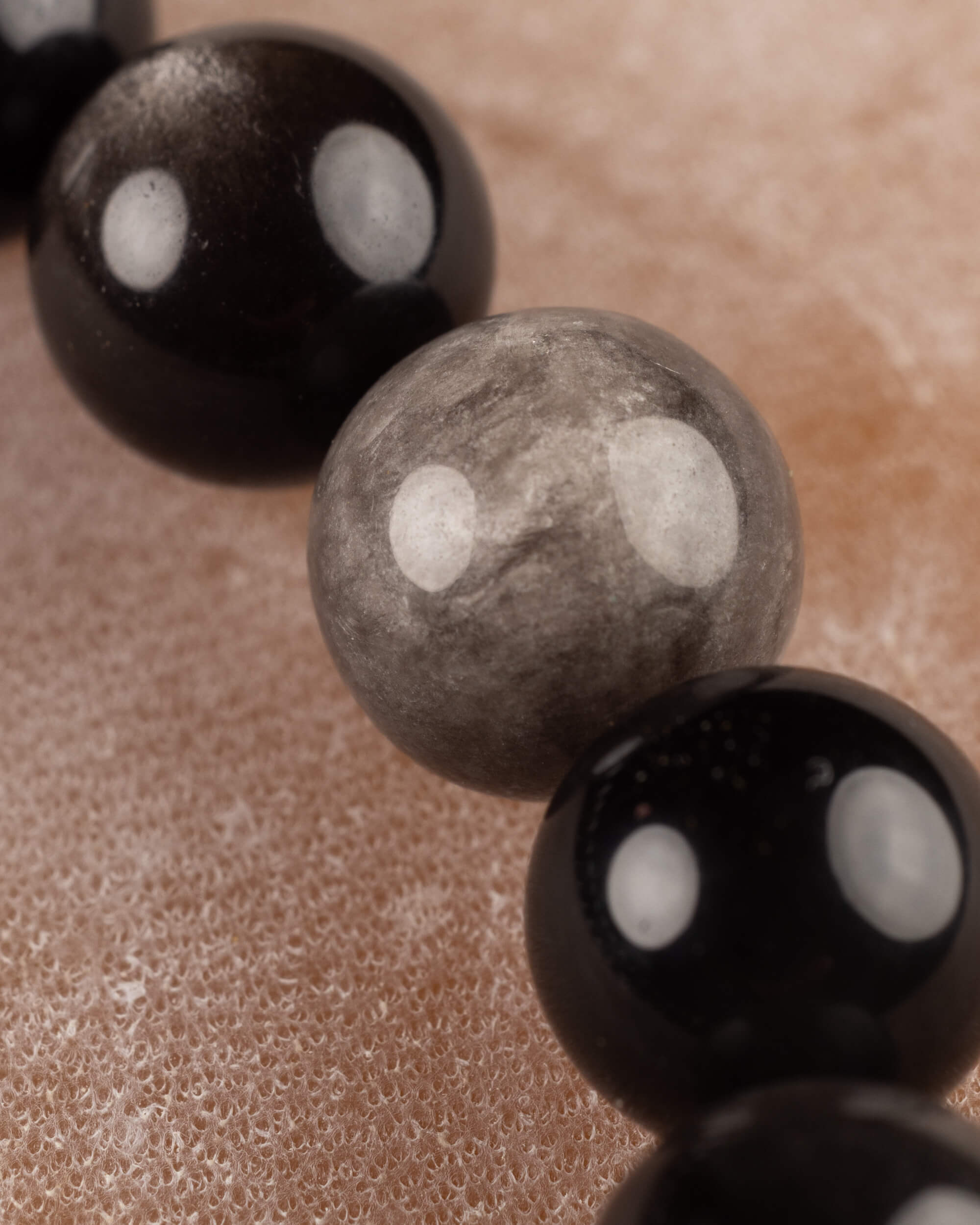 Detalle macro de cuenta gris de Obsidiana Plateada rodeada de cuentas negras
