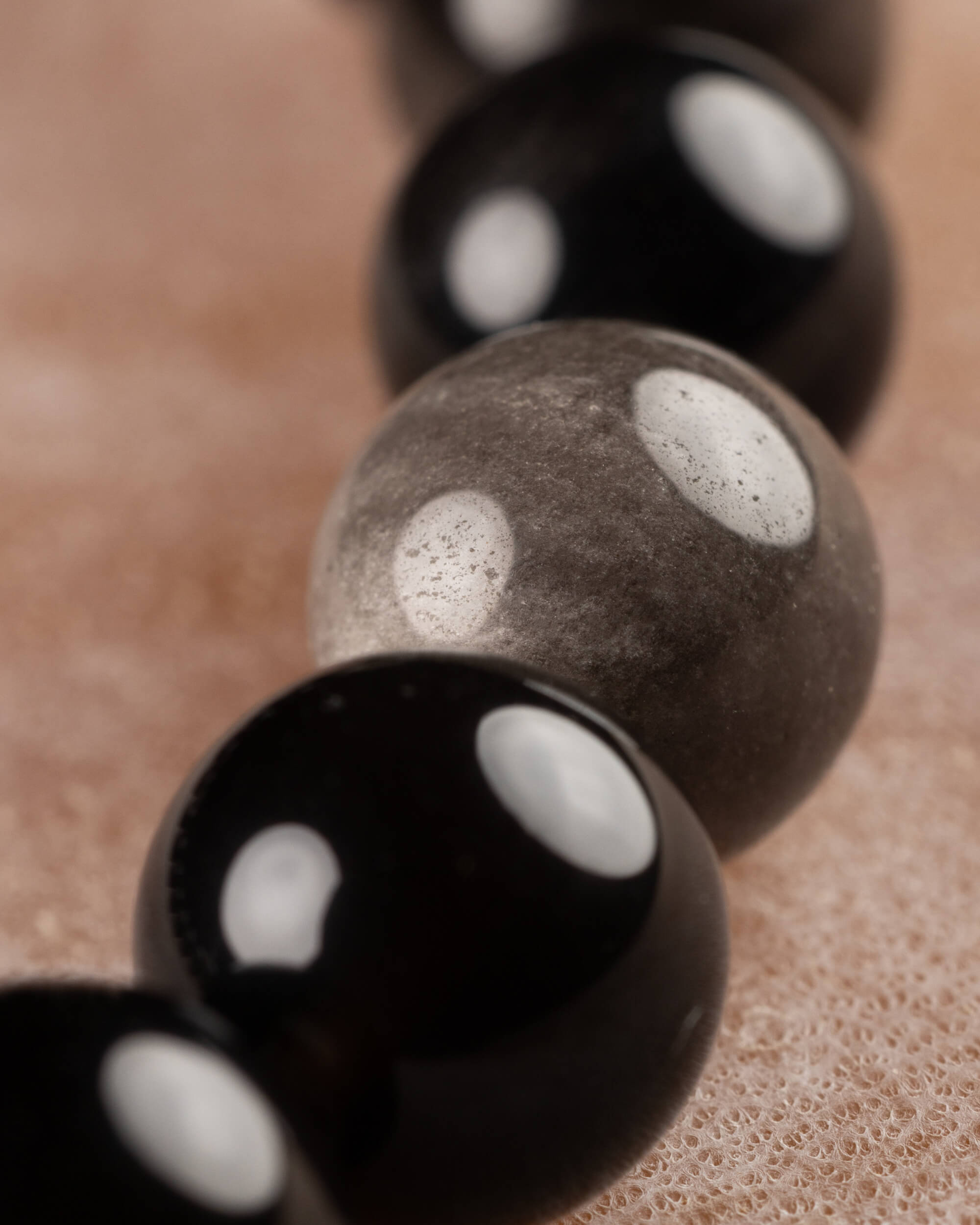 Detalle macro de cuenta gris de Obsidiana Plateada entre cuentas negras brillantes