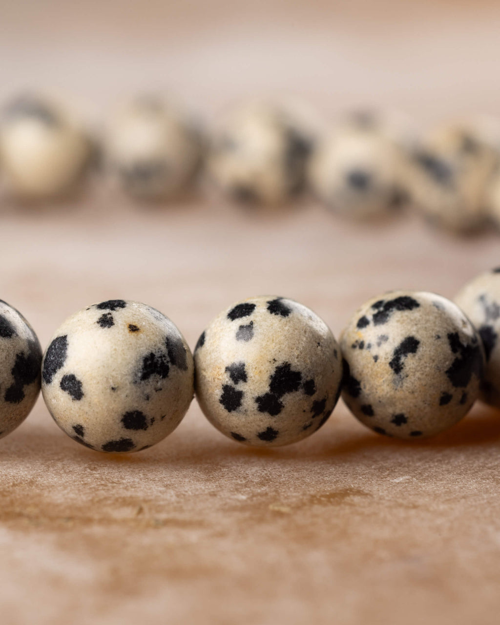 Cuentas de Jaspe Dalmata en fila sobre superficie clara, patron moteado