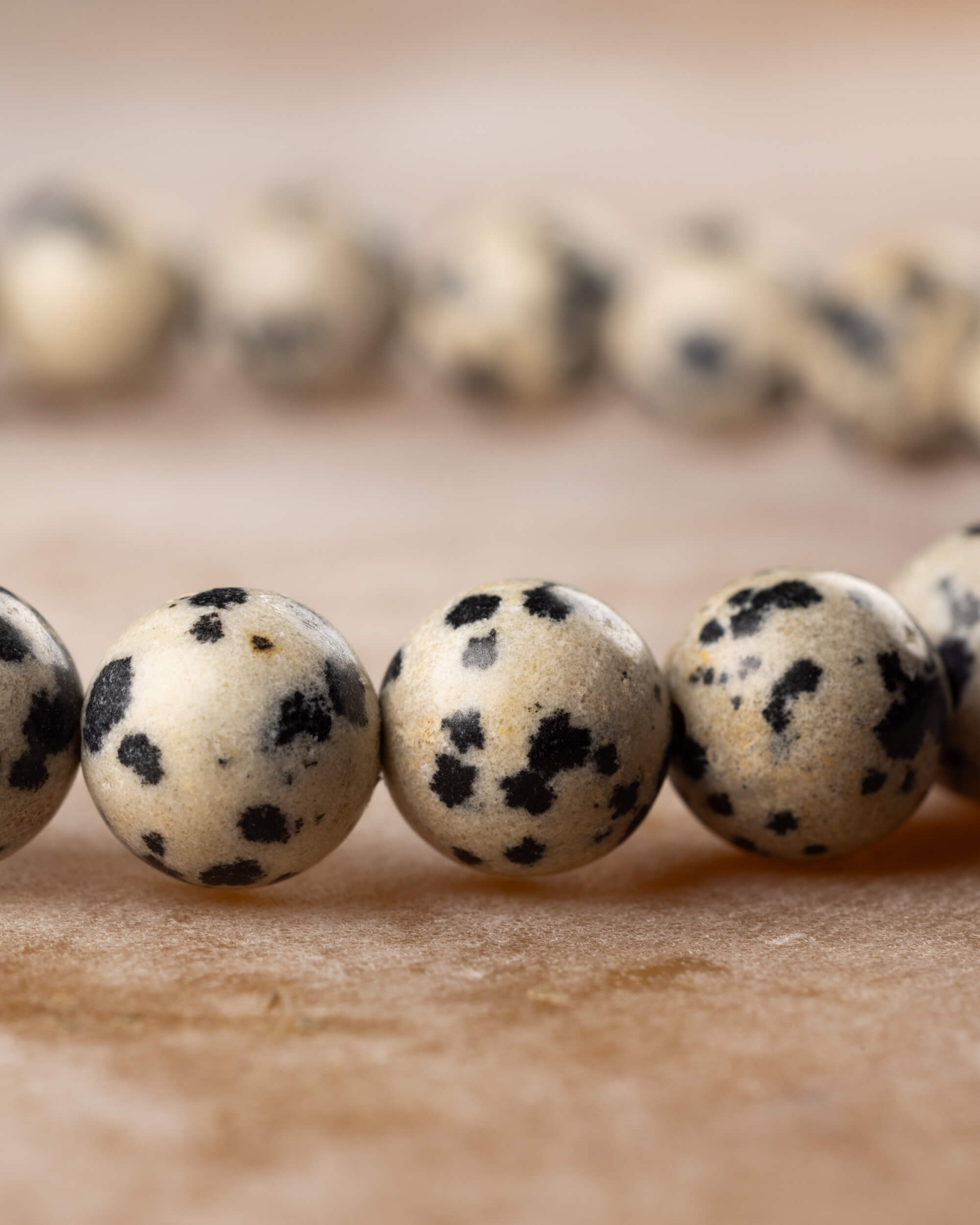 Cuentas de Jaspe Dalmata en fila sobre superficie clara, patron moteado
