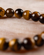 Pulsera de Ojo de Tigre en perspectiva, cuentas doradas en curva sobre superficie clara