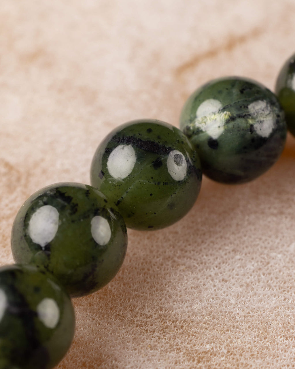 Detalle macro de las cuentas de Jade Verde Oscuro en fila sobre superficie clara