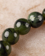 Detalle macro de las cuentas de Jade Verde Oscuro en fila sobre superficie clara