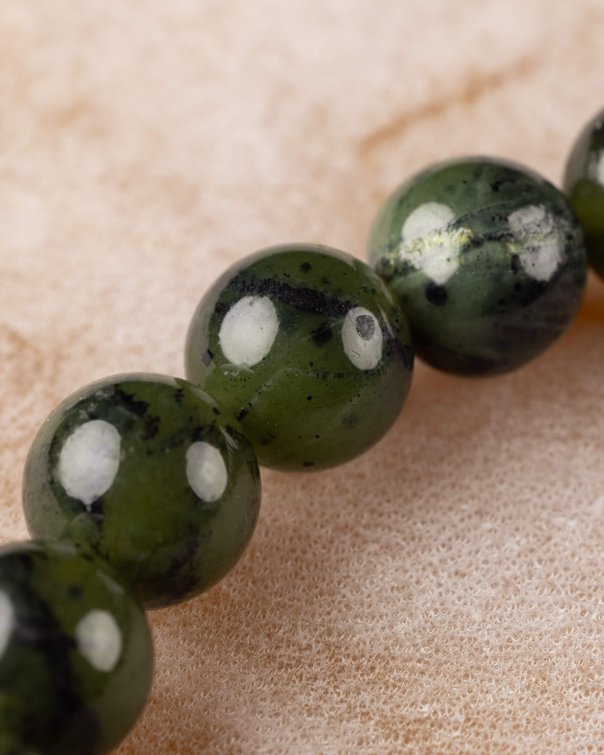 Detalle macro de las cuentas de Jade Verde Oscuro en fila sobre superficie clara