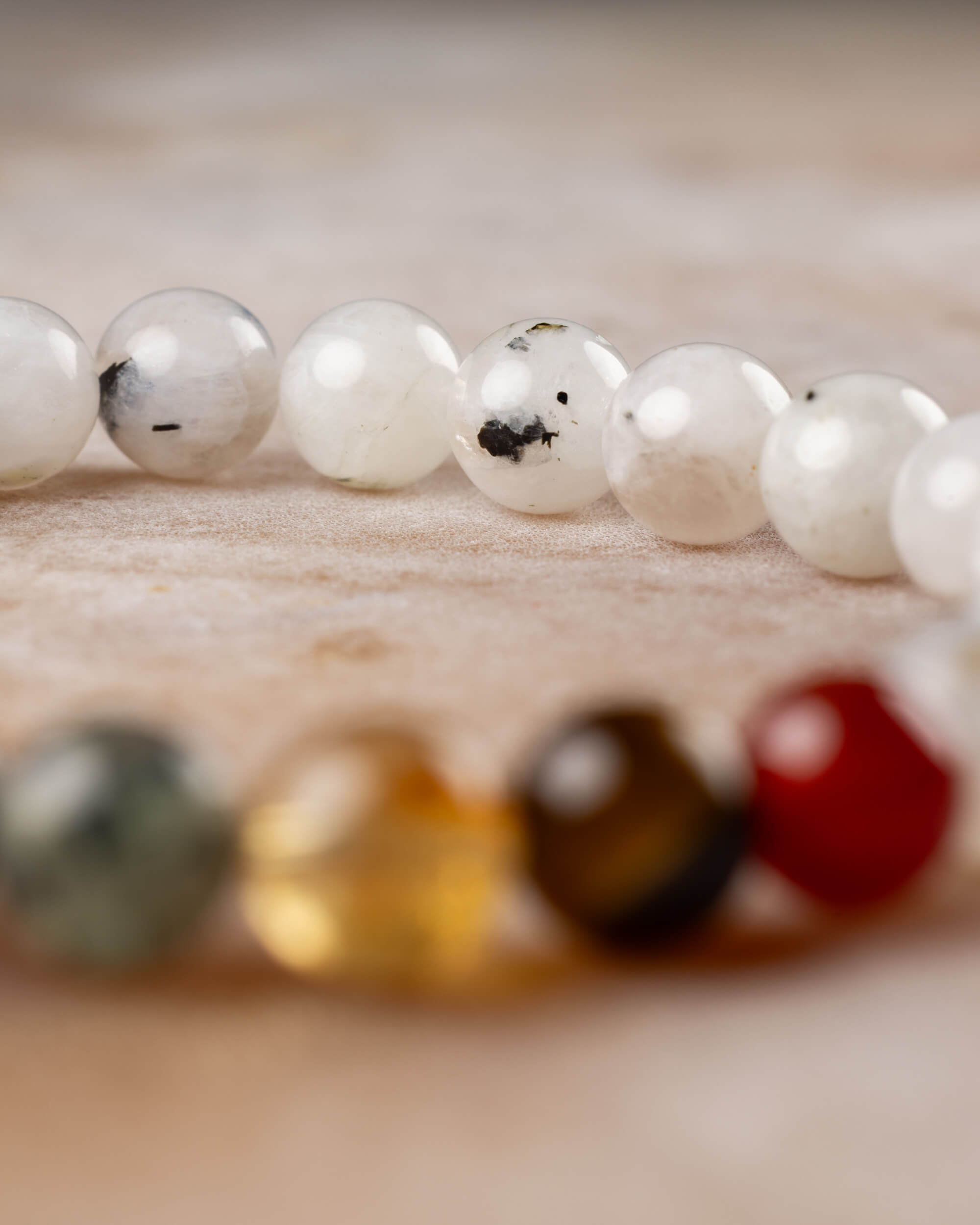 Cuentas de Piedra Luna en fila, con las de los 7 Chakras desenfocadas al fondo