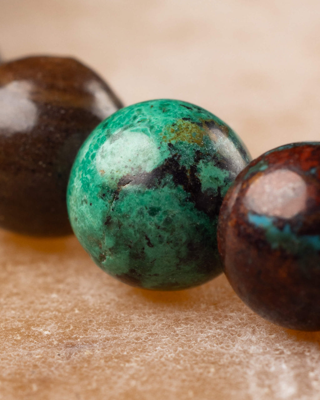 Detalle macro de tres cuentas redondas de Crisocola con vetas verdes y cafes