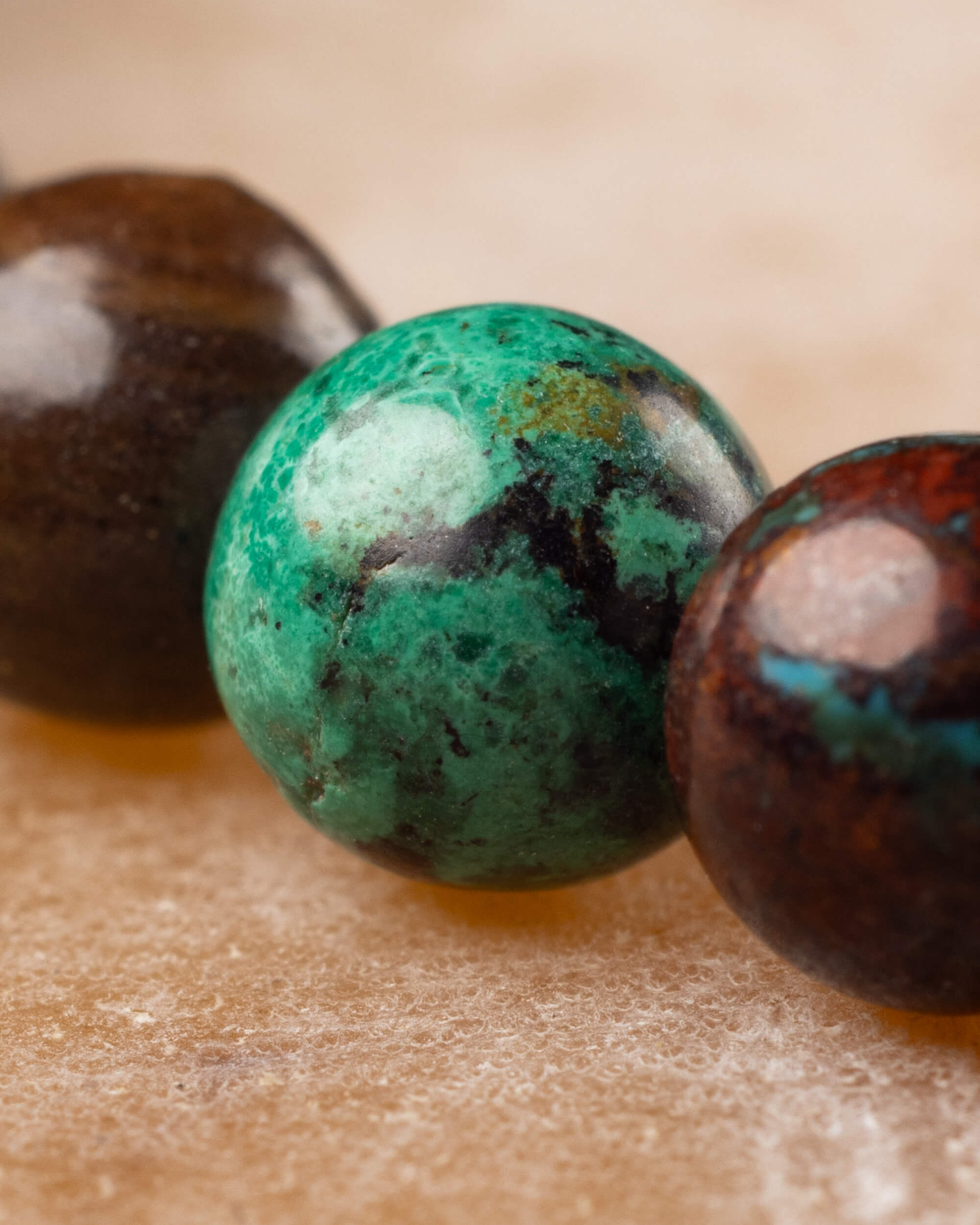Detalle macro de tres cuentas redondas de Crisocola con vetas verdes y cafes