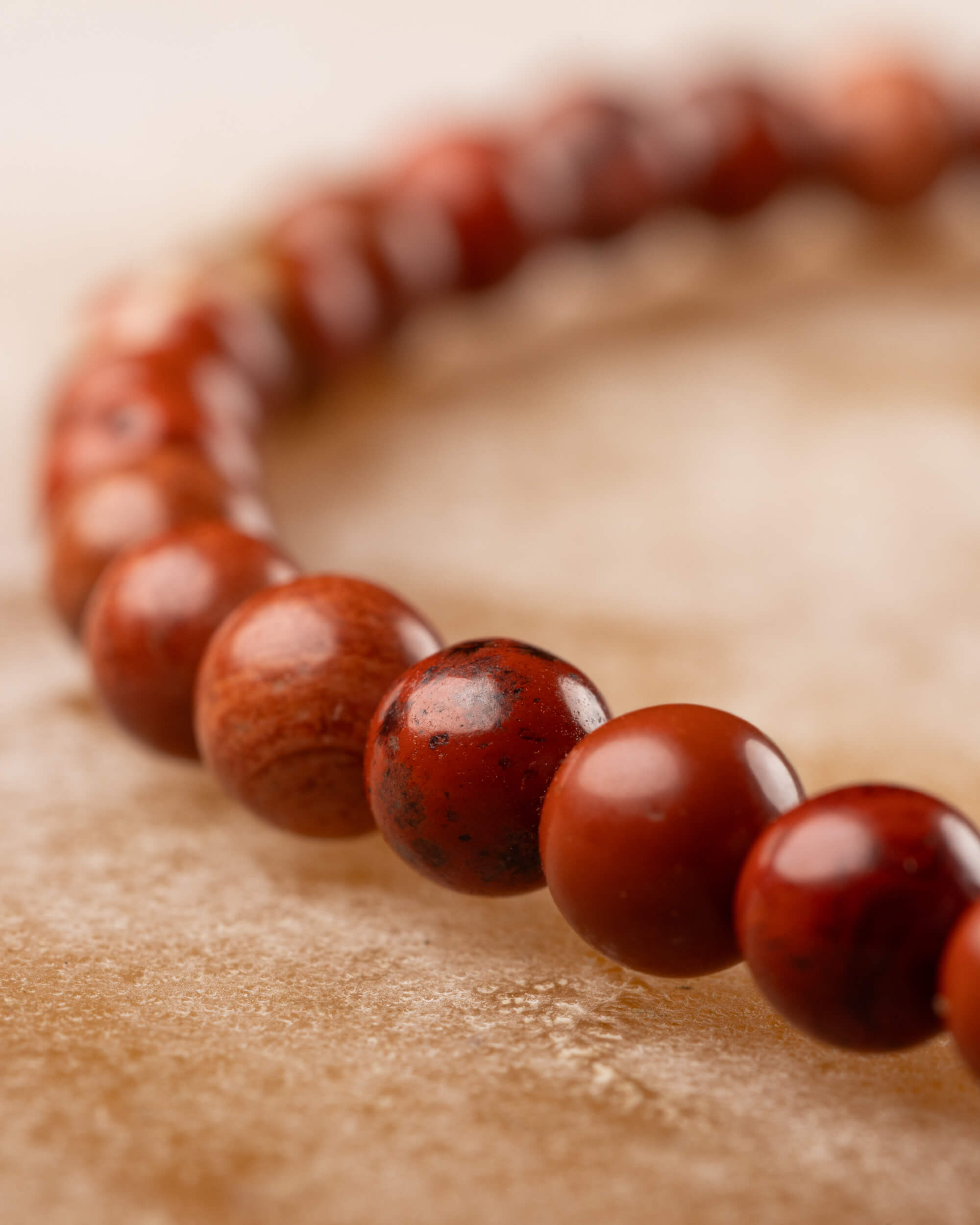 Pulsera de Jaspe Rojo en curva sobre piedra clara, cuentas de tonos rojo y ocre