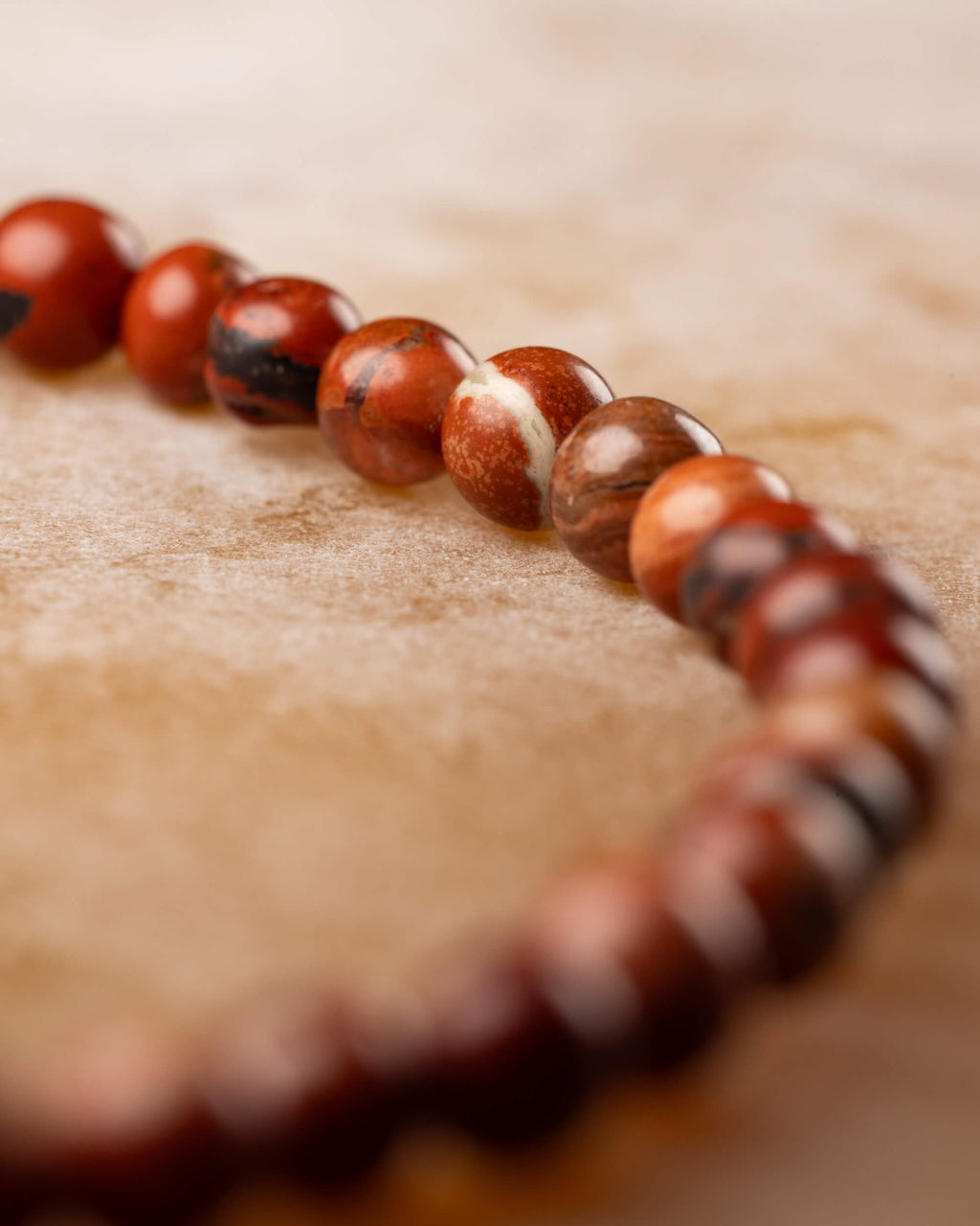 Pulsera de Jaspe Rojo en perspectiva curva, cuentas con vetas claras al frente