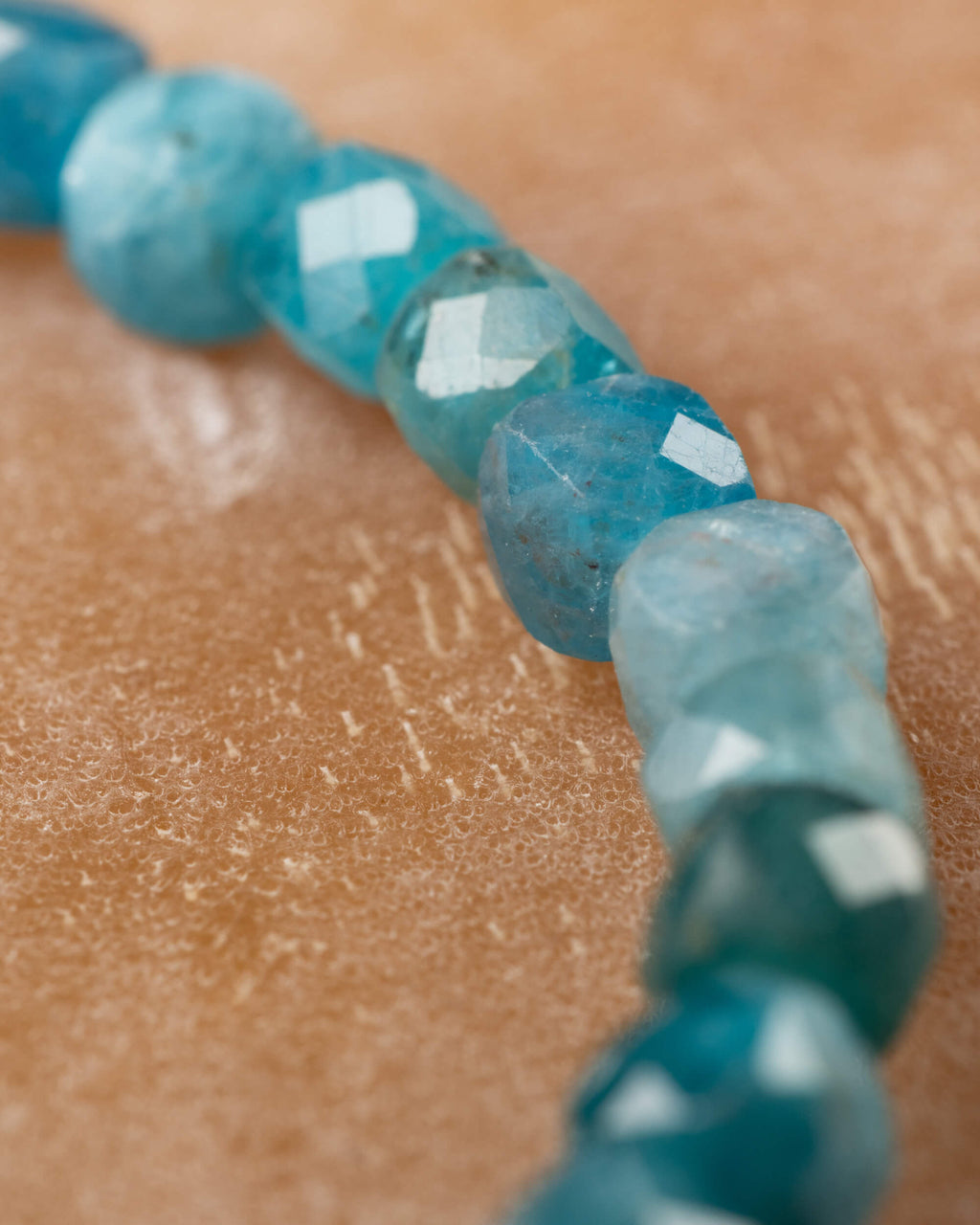 Pulsera de Apatita Azul en curva, angulo cercano sobre superficie clara