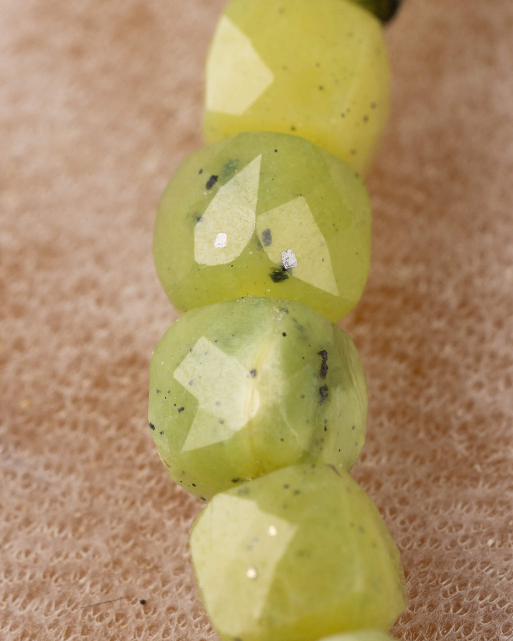 Detalle macro vertical de las cuentas facetadas de Jade Verde con motas oscuras