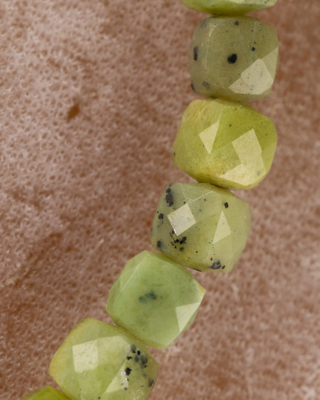 Detalle macro vertical de las cuentas facetadas de Jade Verde con motas oscuras