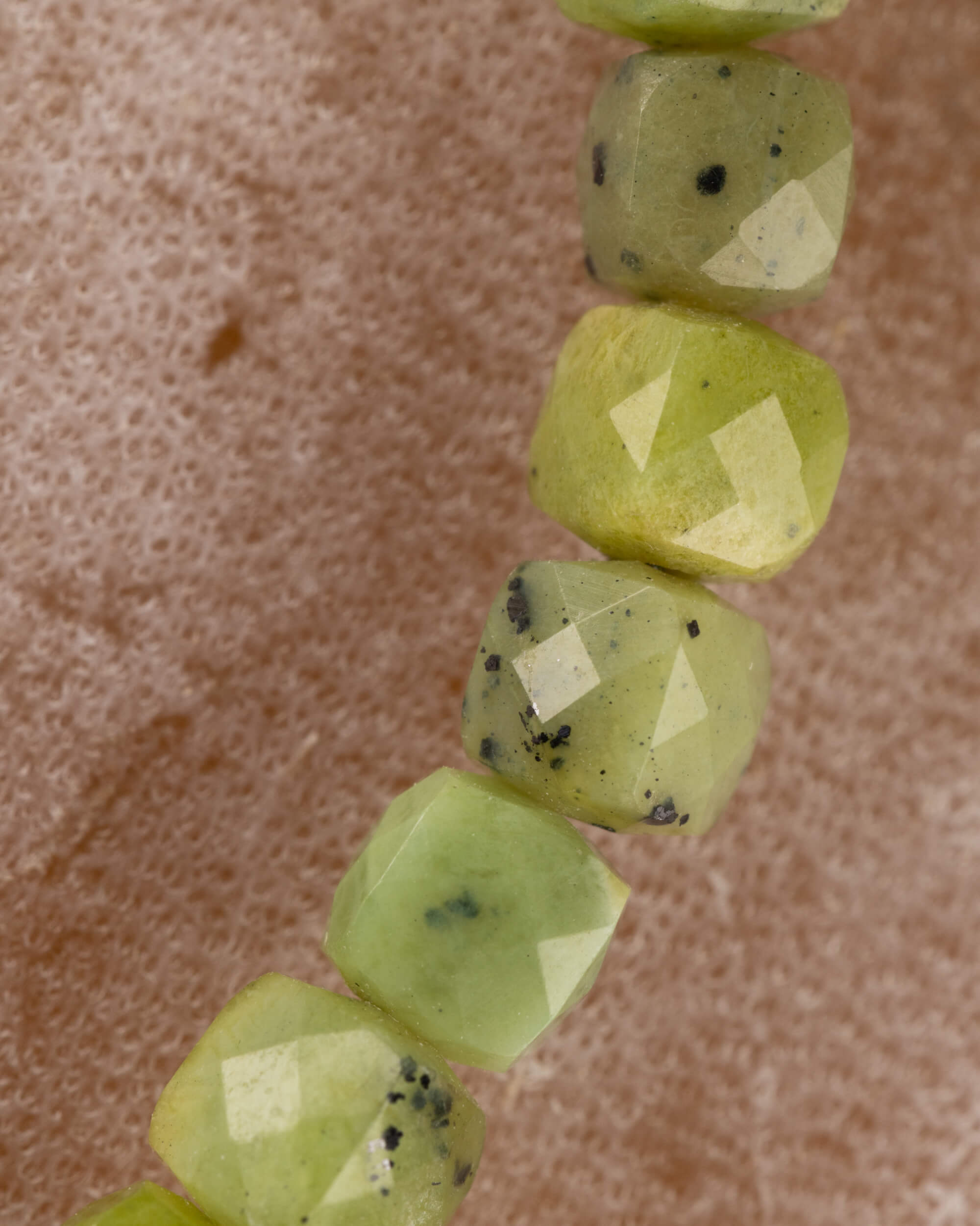 Detalle macro vertical de las cuentas facetadas de Jade Verde con motas oscuras