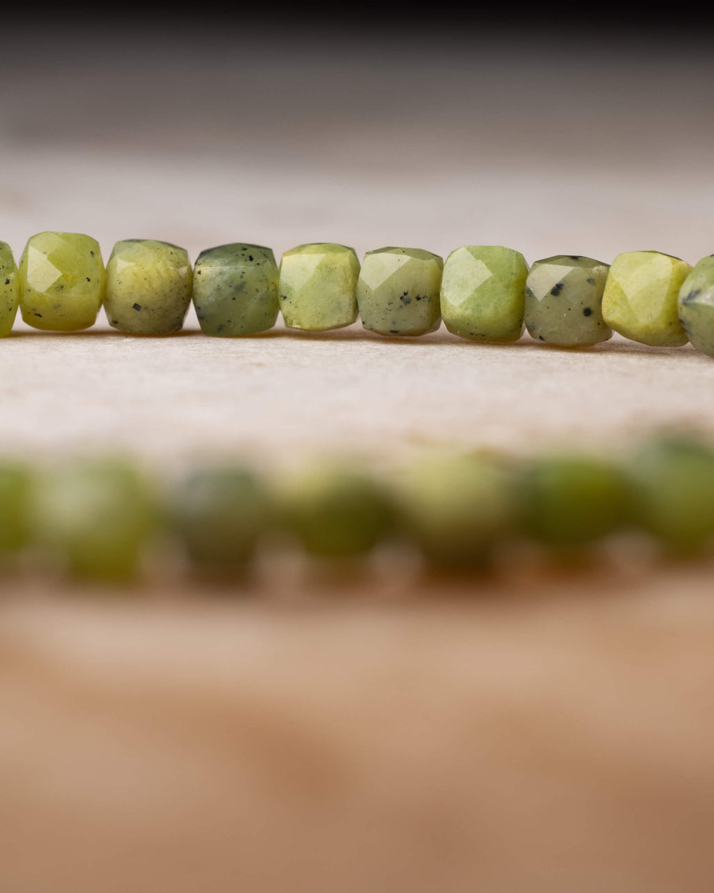 Cuentas de Jade Verde facetadas en fila con el círculo de la pulsera desenfocado al fondo