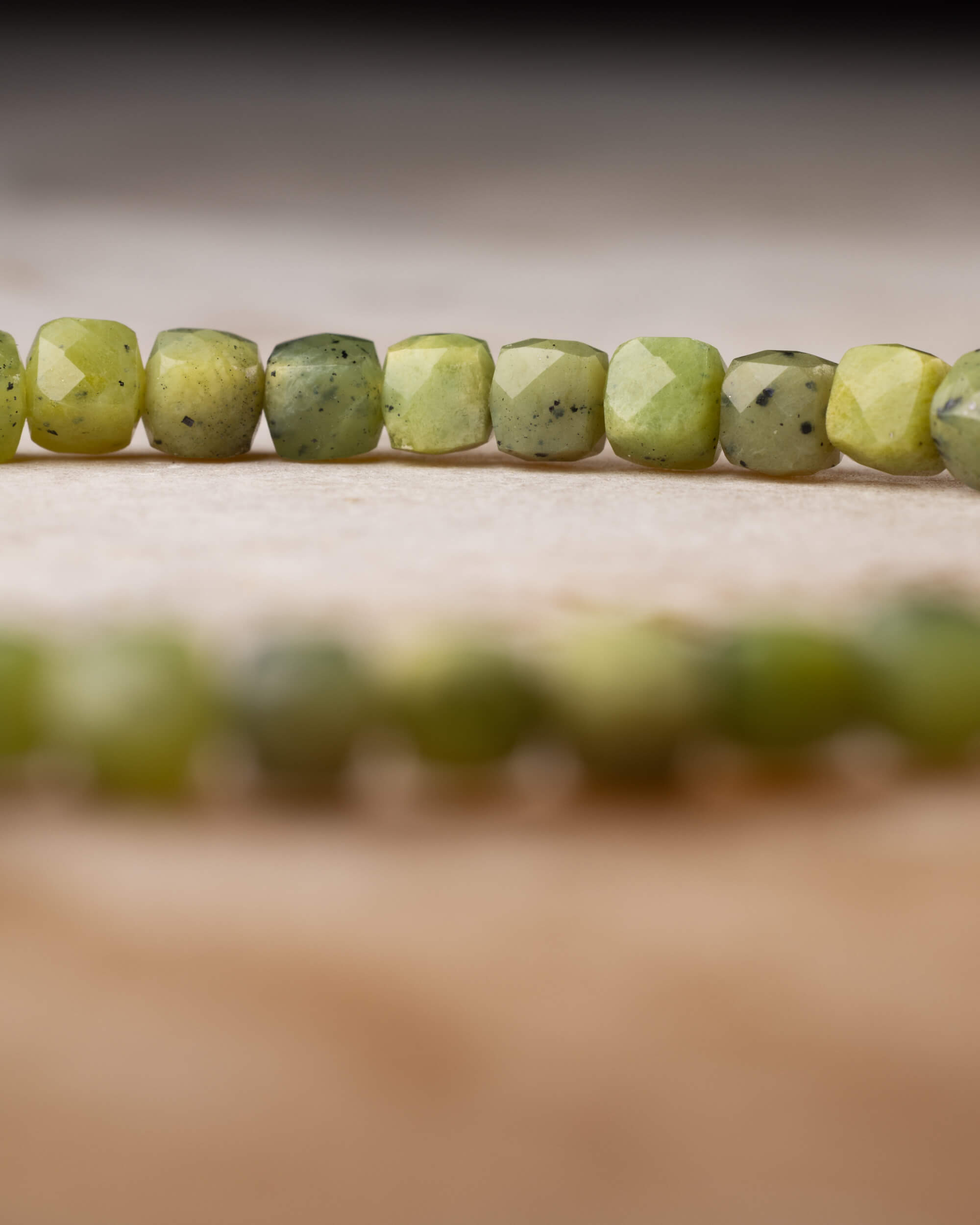 Cuentas de Jade Verde facetadas en fila con el círculo de la pulsera desenfocado al fondo