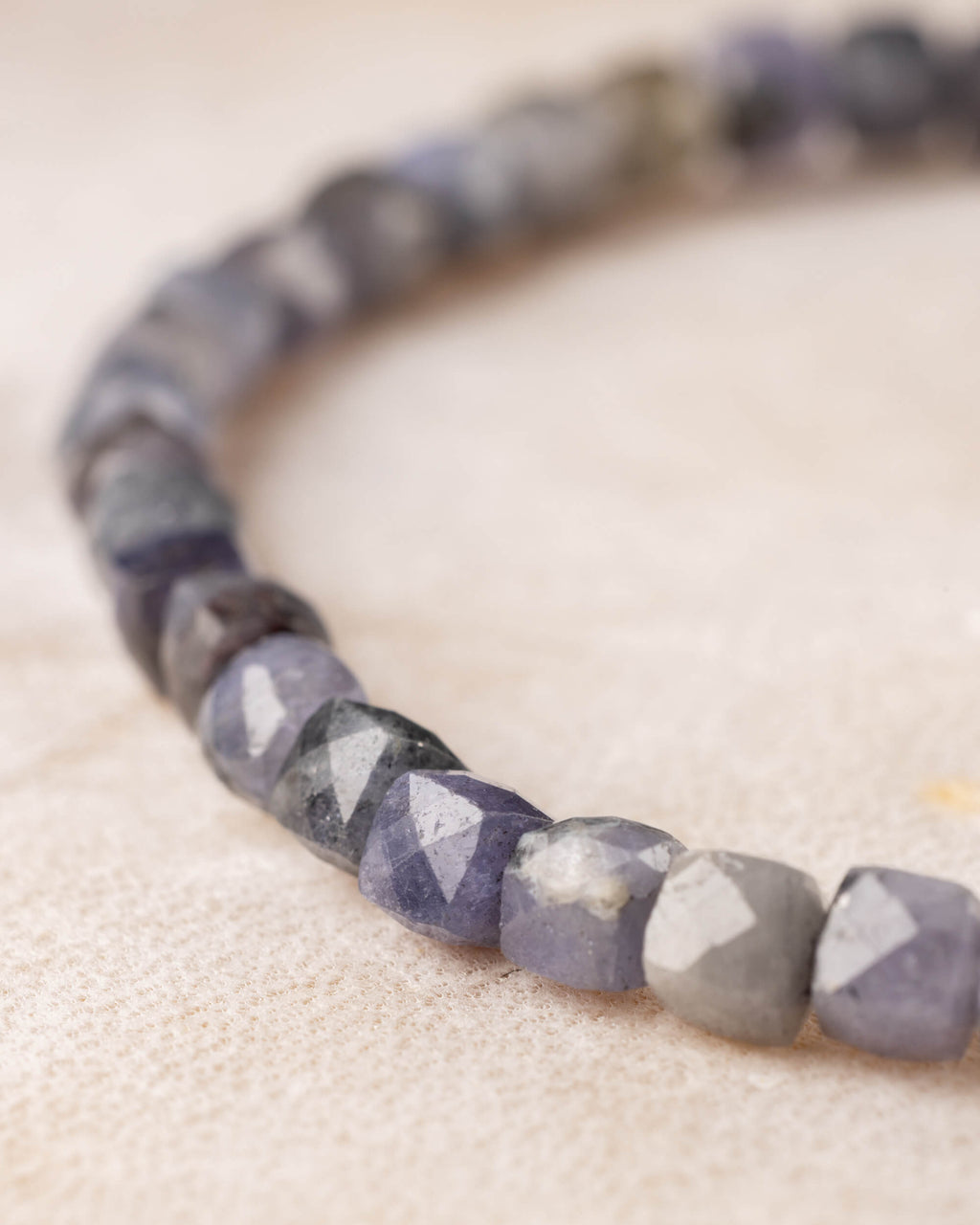 Pulsera de Tanzanita en perspectiva, curva de cuentas facetadas sobre madera clara