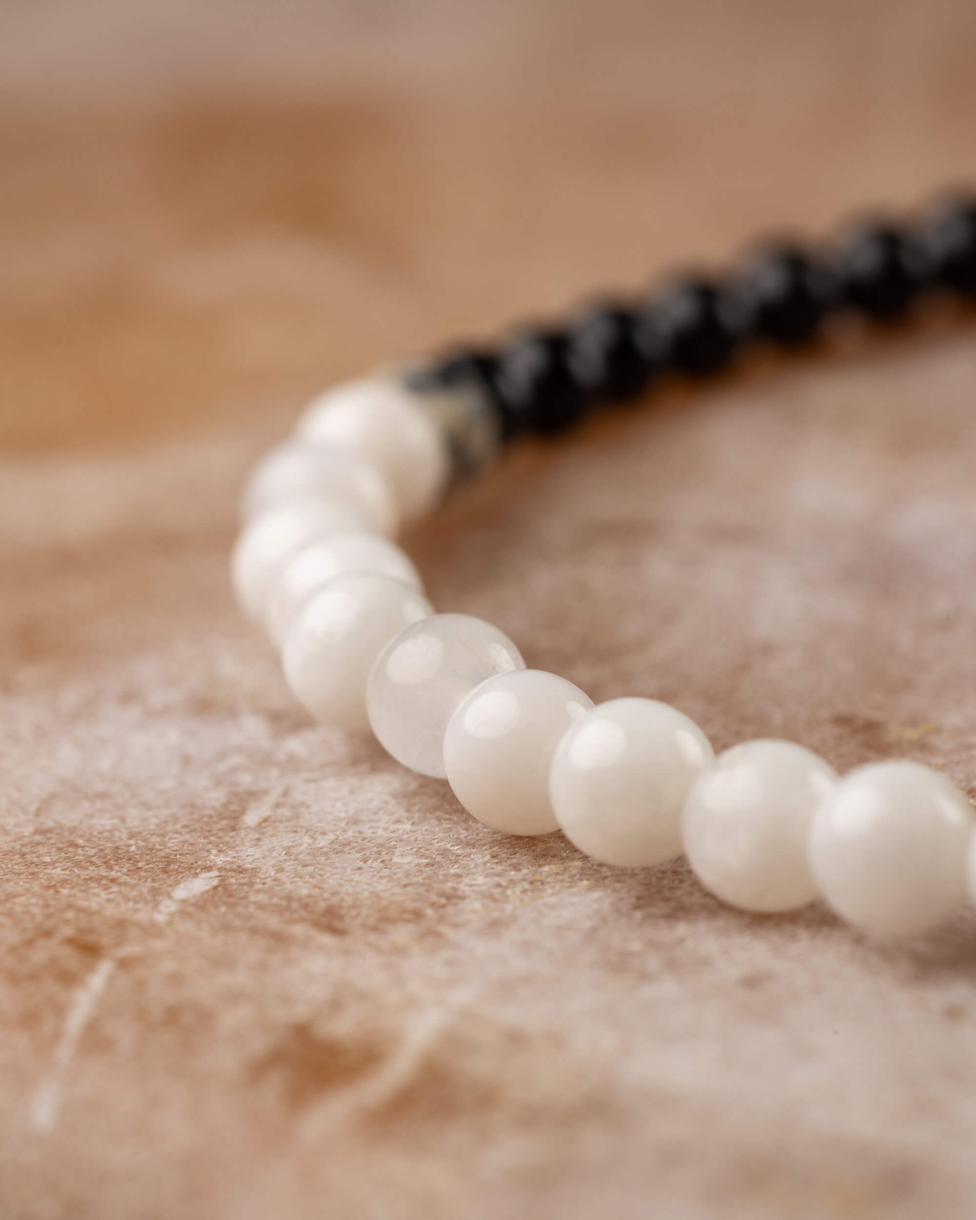 Detalle macro de las cuentas de Piedra Luna con hilo de Turmalina Negra al fondo, pulsera Unidad