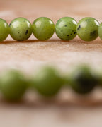 Pulsera de Jade Verde en perspectiva con hilera de cuentas en fondo desenfocado