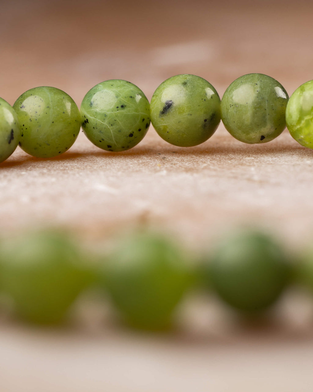 Pulsera de Jade Verde en perspectiva con anillo de cuentas al fondo desenfocado