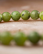Pulsera de Jade Verde en perspectiva con anillo de cuentas al fondo desenfocado