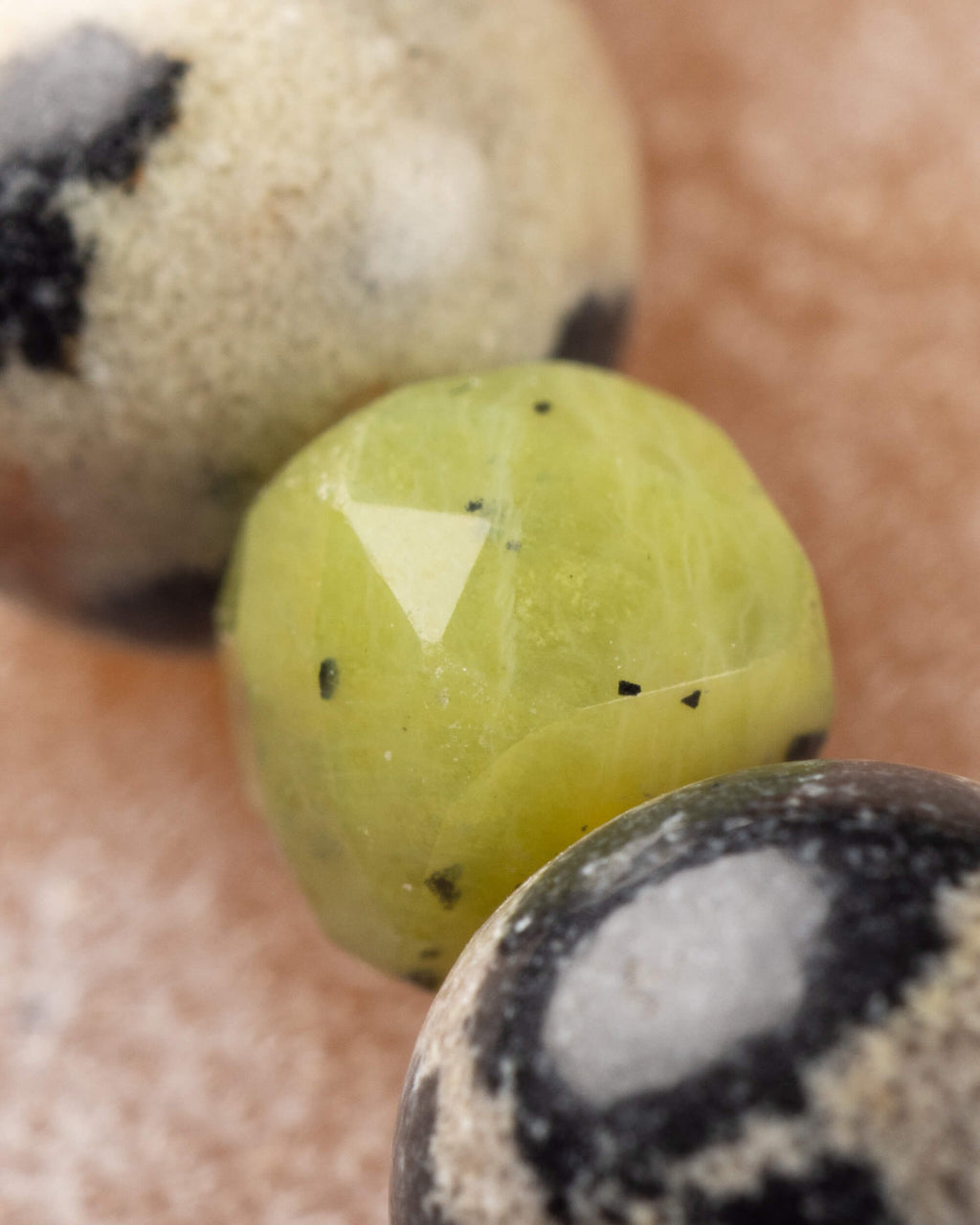 Detalle macro extremo de una cuenta facetada de Jade Verde entre dos cuentas de Jaspe Dálmata