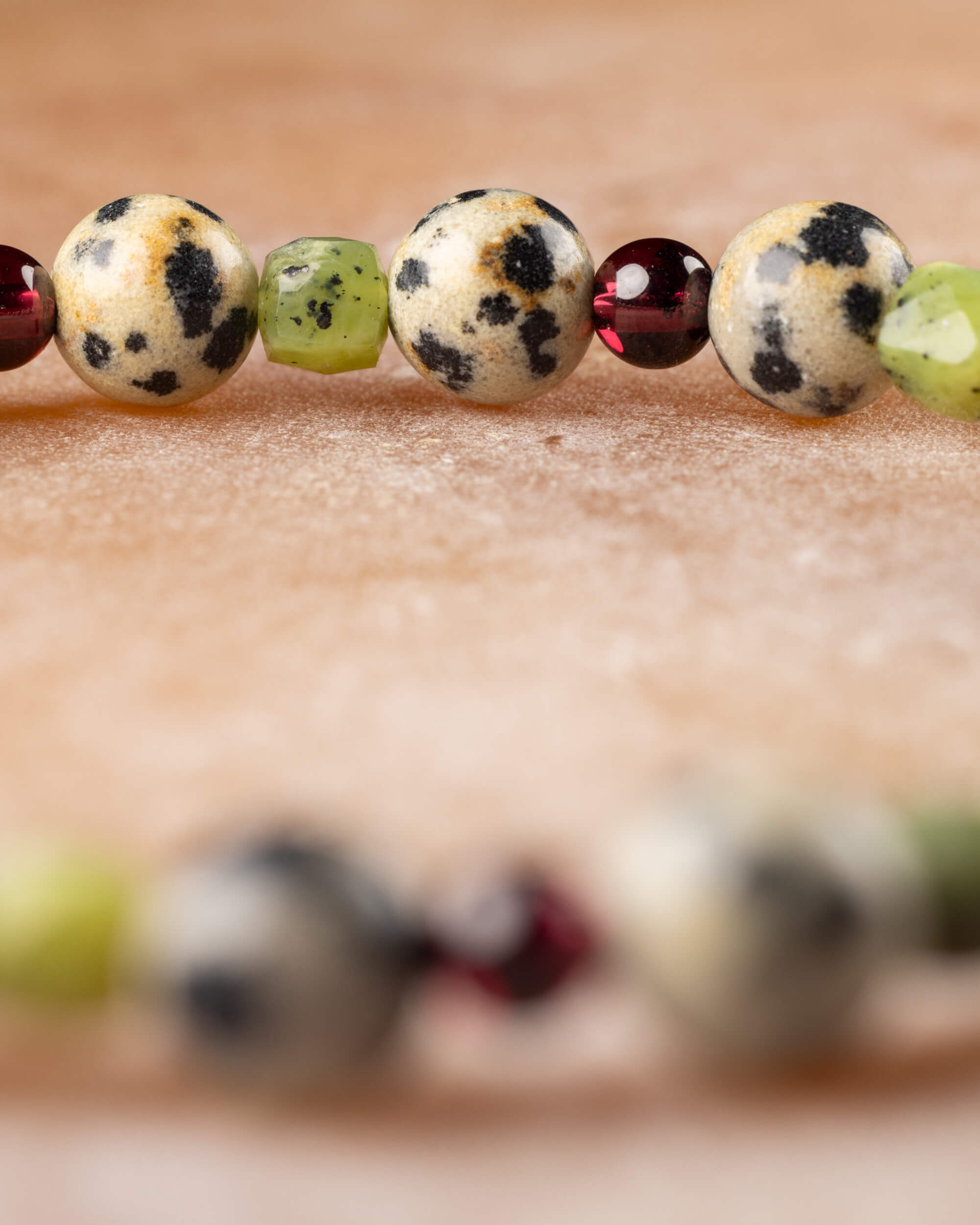 Detalle macro de las cuentas de Jaspe Dálmata, Jade Verde y Granate con fondo desenfocado de la pulsera