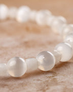 Pulsera de cuentas blancas de Selenita y Piedra Luna puesta en la muneca, brillo suave, sin relieve visible