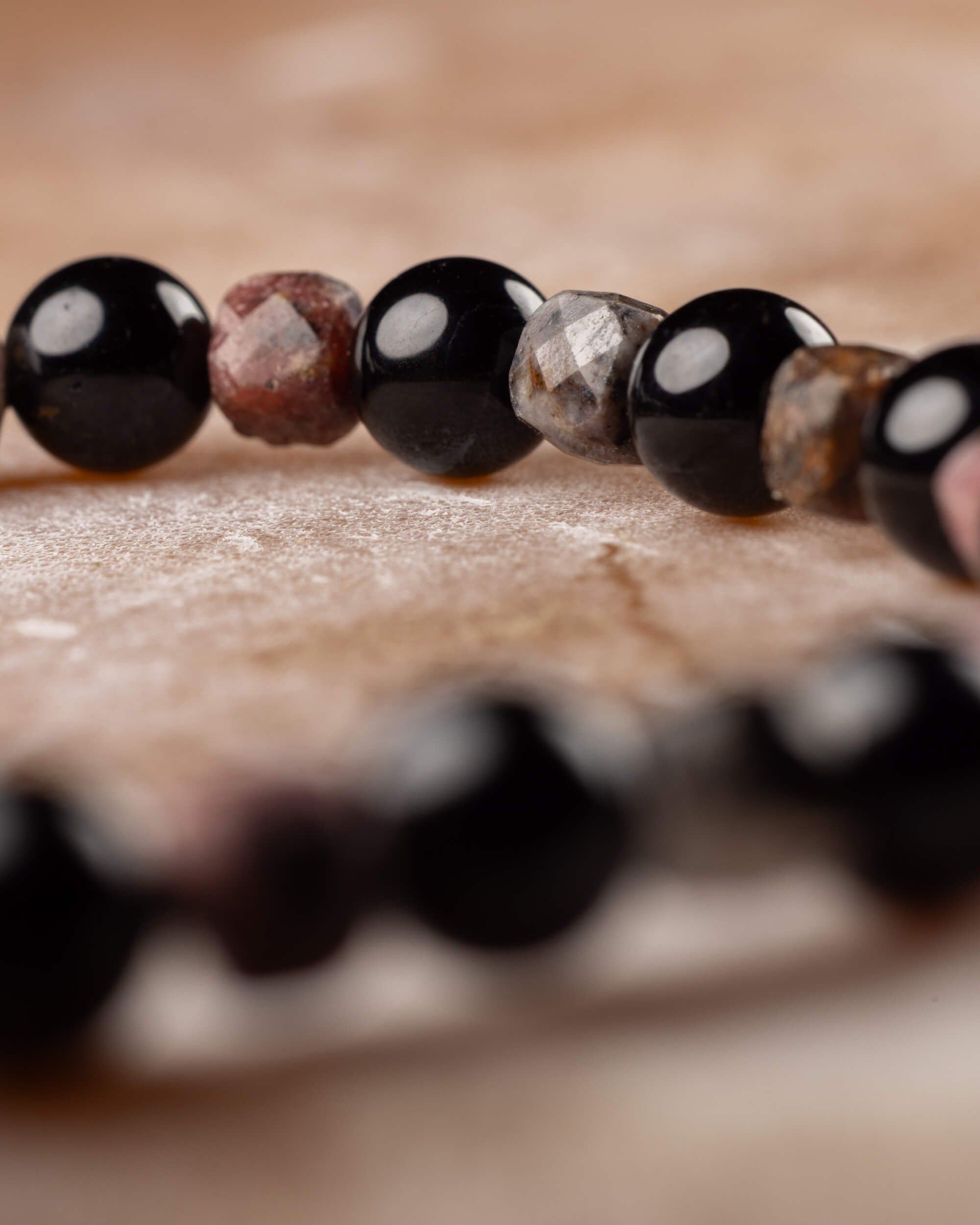 Cuentas de Turmalina Negra y Rodonita facetada en fila, con el círculo de la pulsera desenfocado al fondo