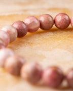 Pulsera de Rodonita Rosa vista de perfil, cuentas en curva sobre superficie dorada
