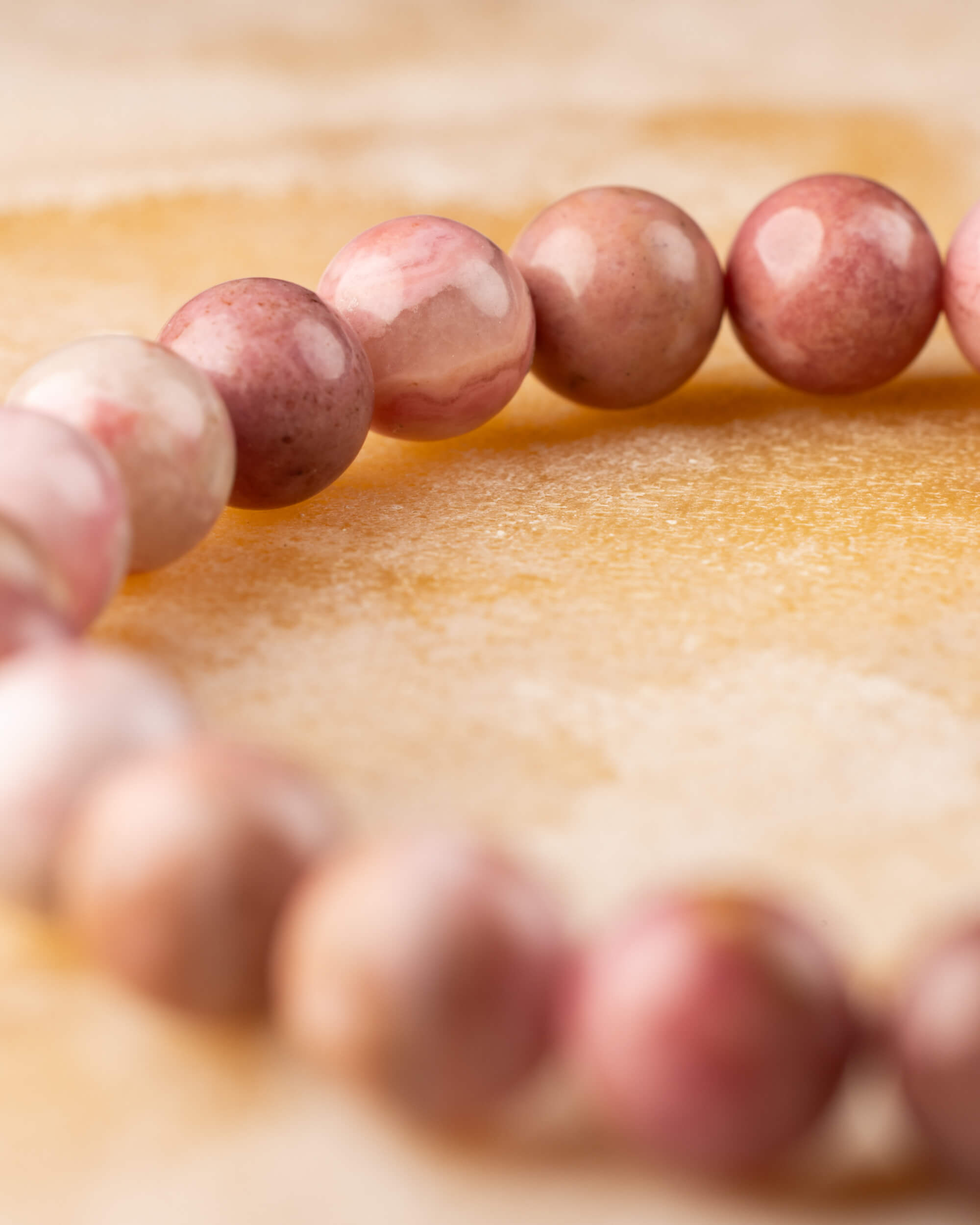 Pulsera de Rodonita Rosa vista de perfil, cuentas en curva sobre superficie dorada