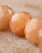 Detalle macro de las cuentas facetadas de Piedra Sol Naranja sobre tela clara
