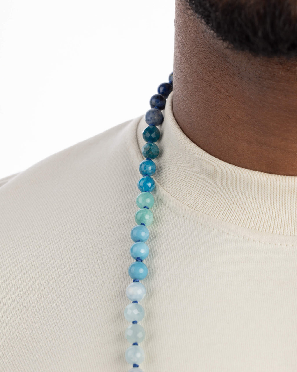 Detalle macro de cuentas azules y turquesas en degradado sobre el cuello, del Japa Mala Universo