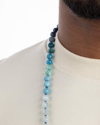 Detalle macro de cuentas azules y turquesas en degradado sobre el cuello, del Japa Mala Universo