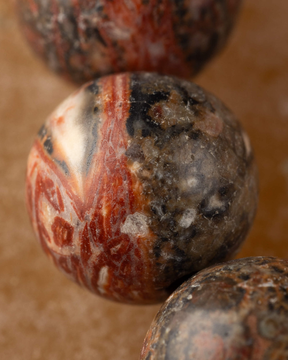 Detalle macro de una cuenta de Jaspe Piel de Leopardo con vetas rojas y negras sobre fondo café claro