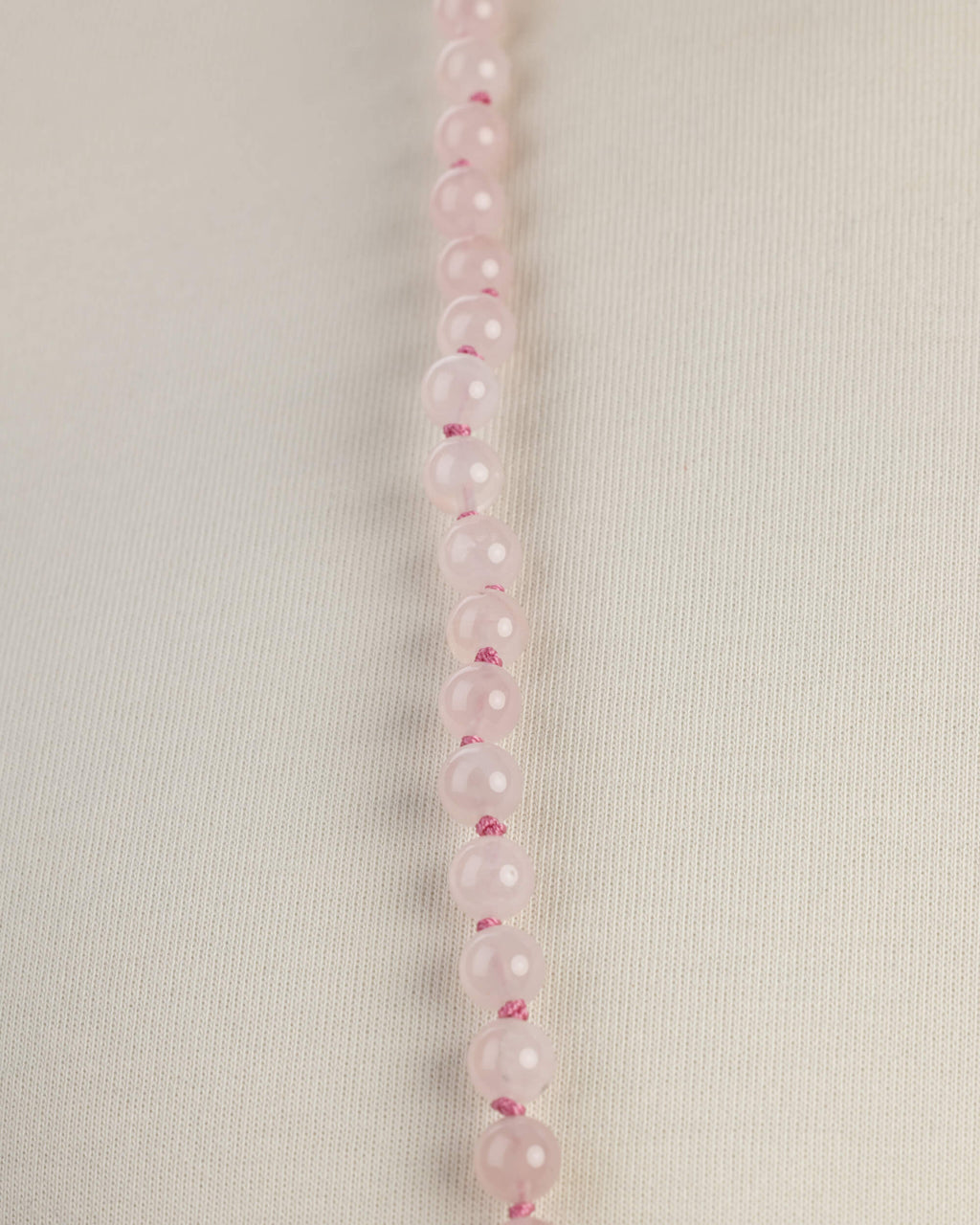 Detalle macro de una hilera de cuentas de Cuarzo Rosa sobre tela clara