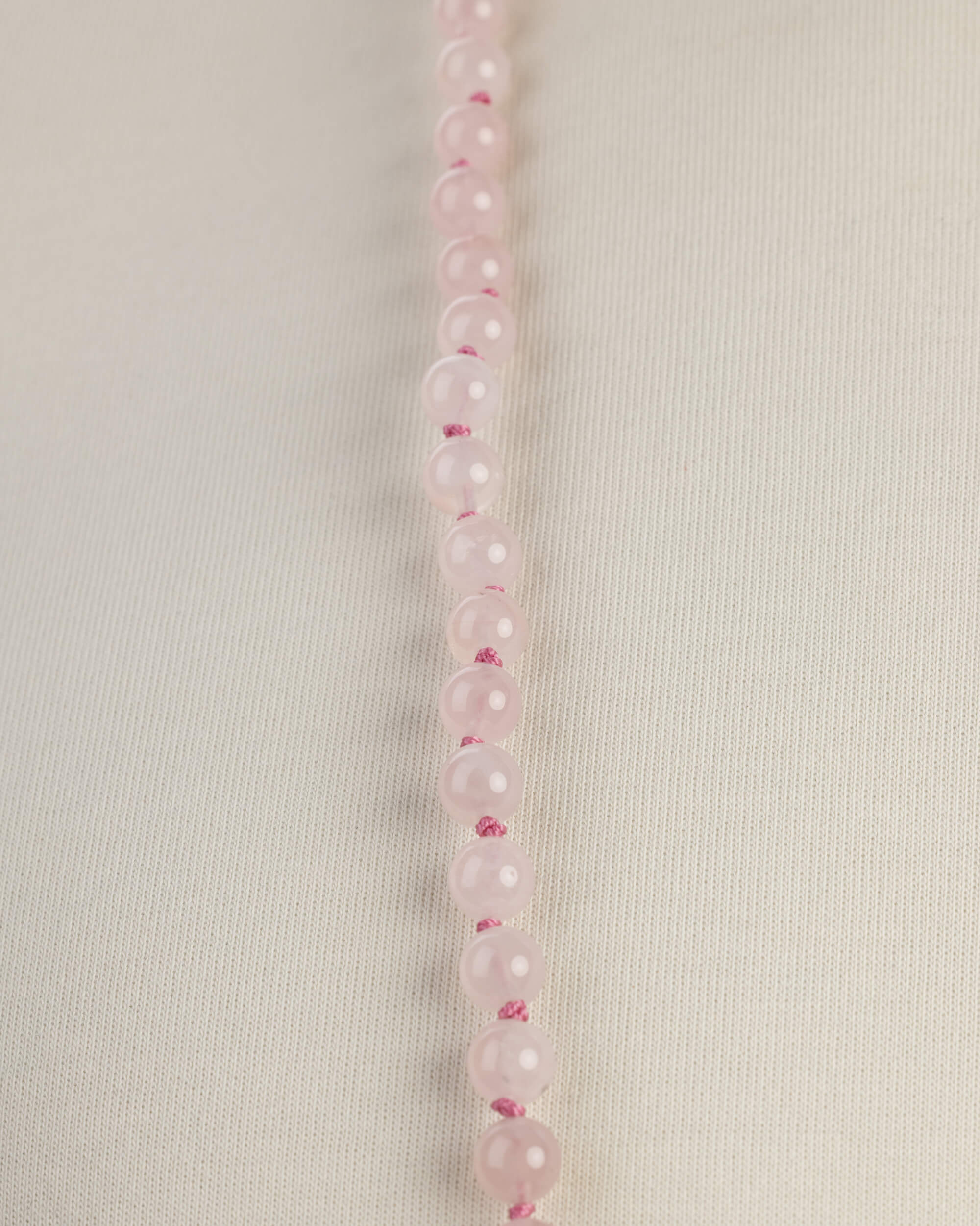 Detalle macro de una hilera de cuentas de Cuarzo Rosa sobre tela clara