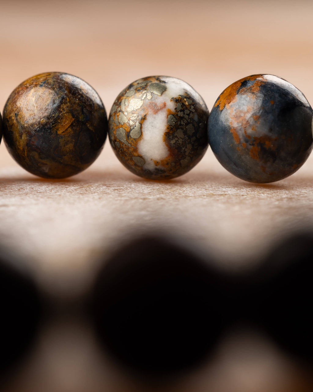 Detalle macro de tres cuentas de Pietersita con vetas doradas, blancas y azuladas