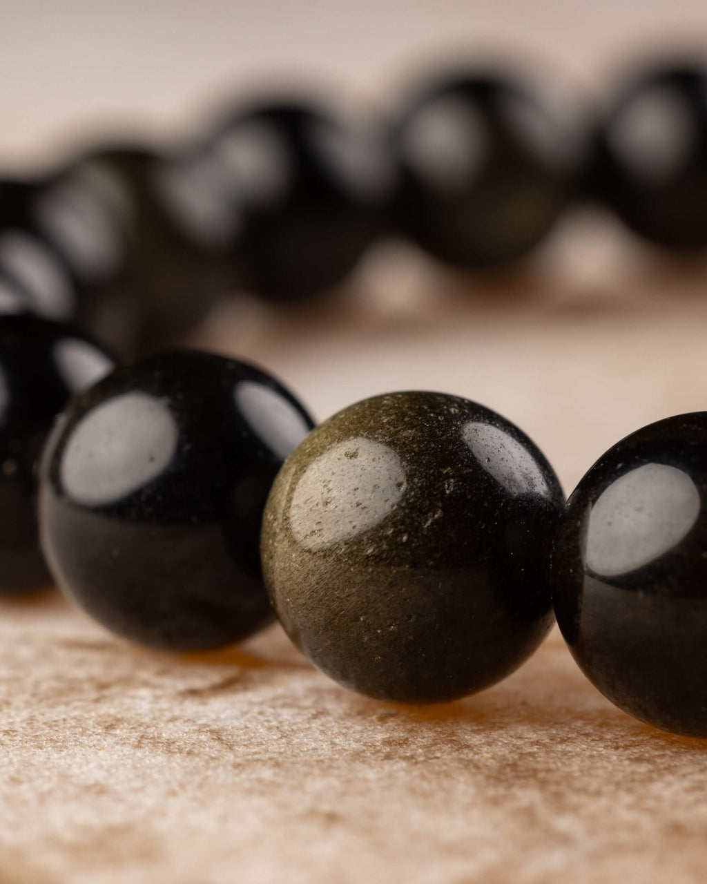 Pulsera de Obsidiana Dorada vista en fila, brillo dorado entre cuentas negras