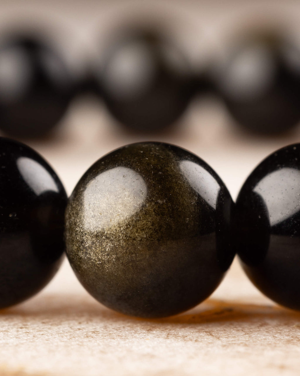 Cuentas de Obsidiana Dorada de frente, brillo dorado sobre superficie de madera clara