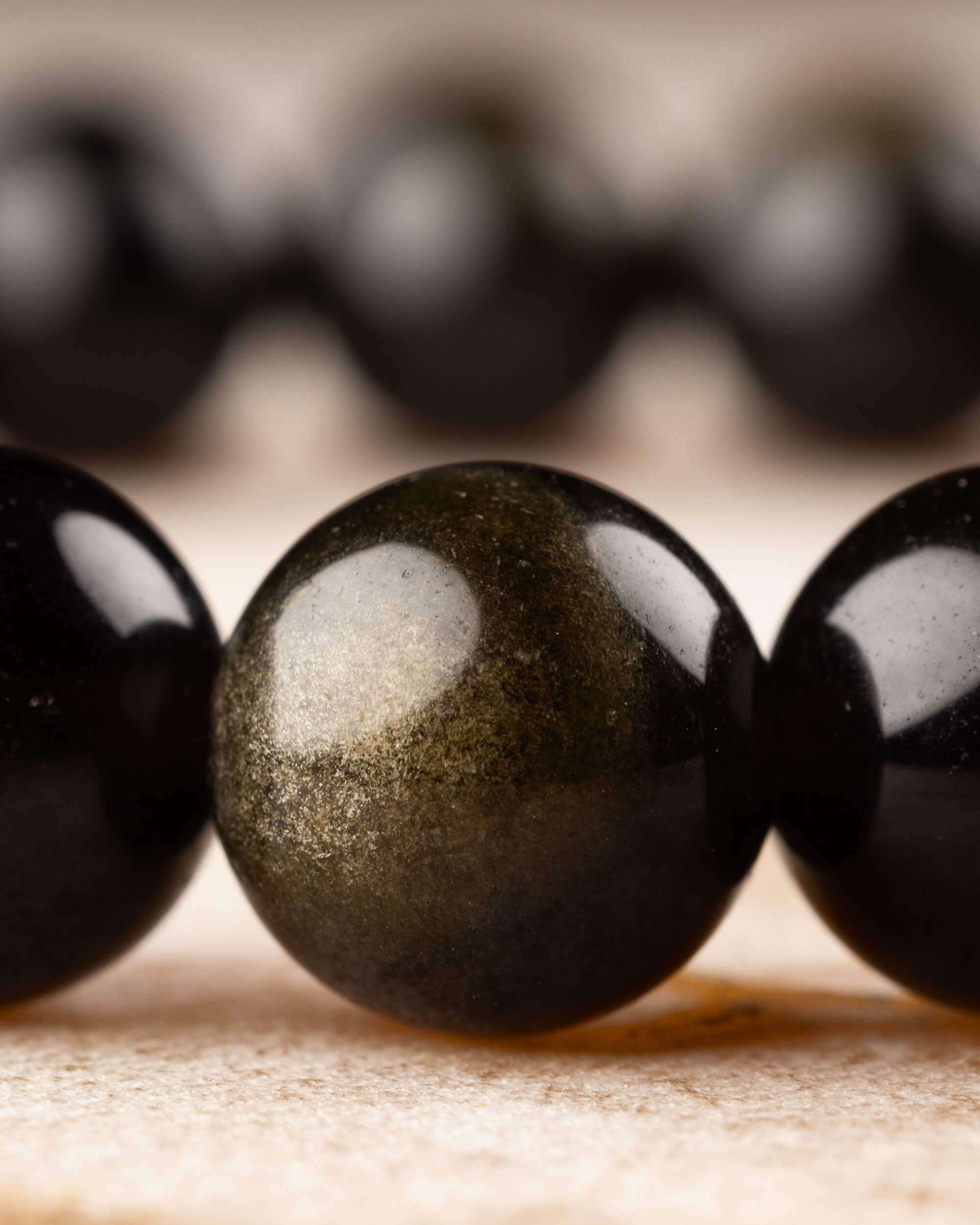Cuentas de Obsidiana Dorada de frente, brillo dorado sobre superficie de madera clara