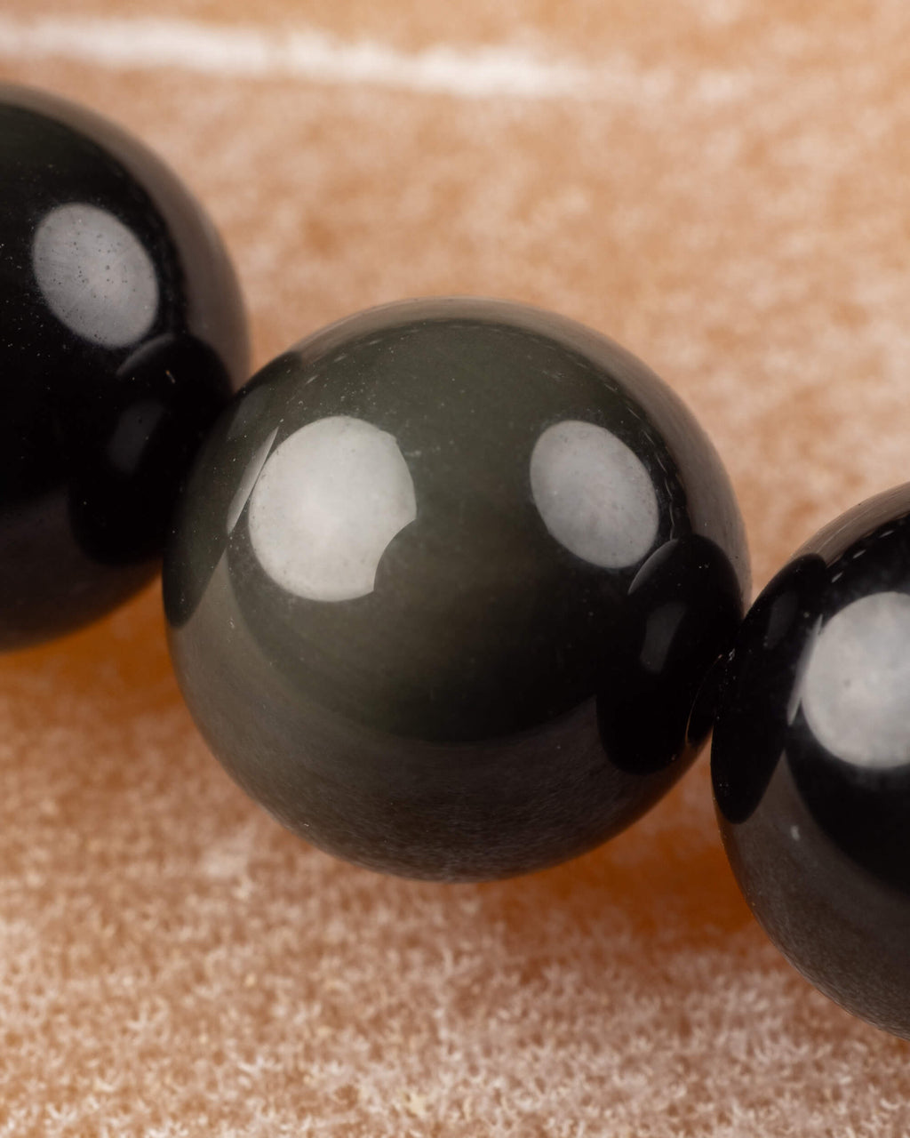 Detalle macro de cuenta de Obsidiana Arcoíris con destello verde entre cuentas negras
