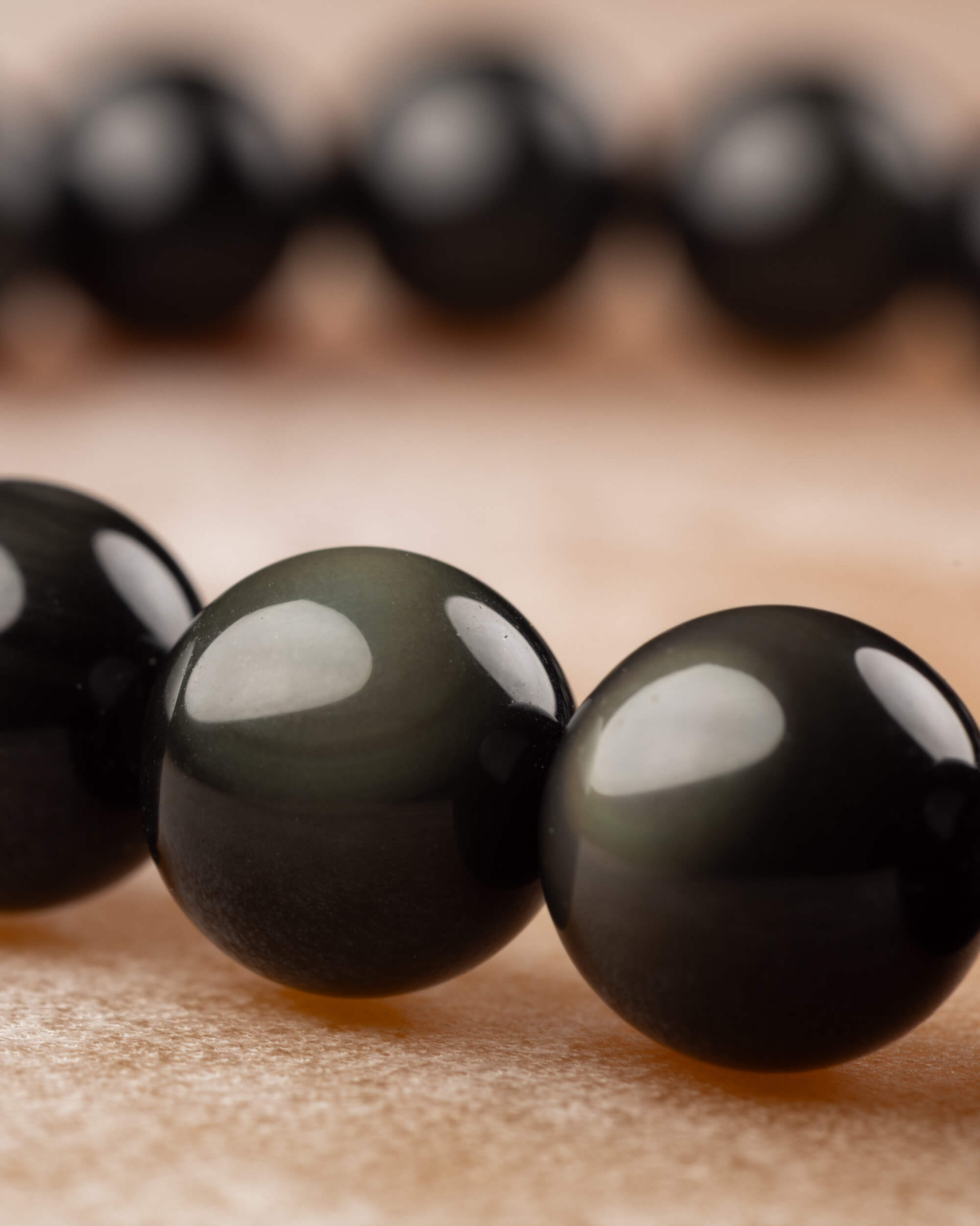 Detalle macro de cuentas de Obsidiana Arcoíris, con destello verdoso característico