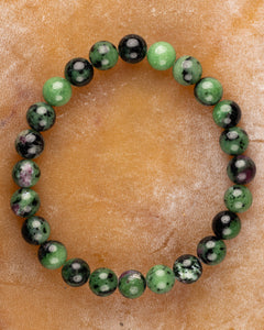 Pulsera de Zoisita completa en círculo sobre superficie color canela, cuentas verdes y negras