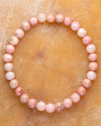 Pulsera de Rodonita Rosa de 6 mm, pieza completa en círculo sobre superficie dorada clara