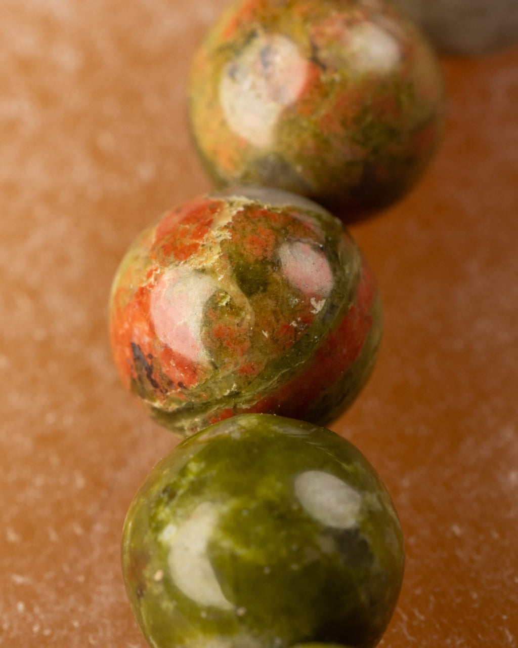 Detalle cercano de una cuenta de Jaspe Unakita con vetas naranjas y verdes